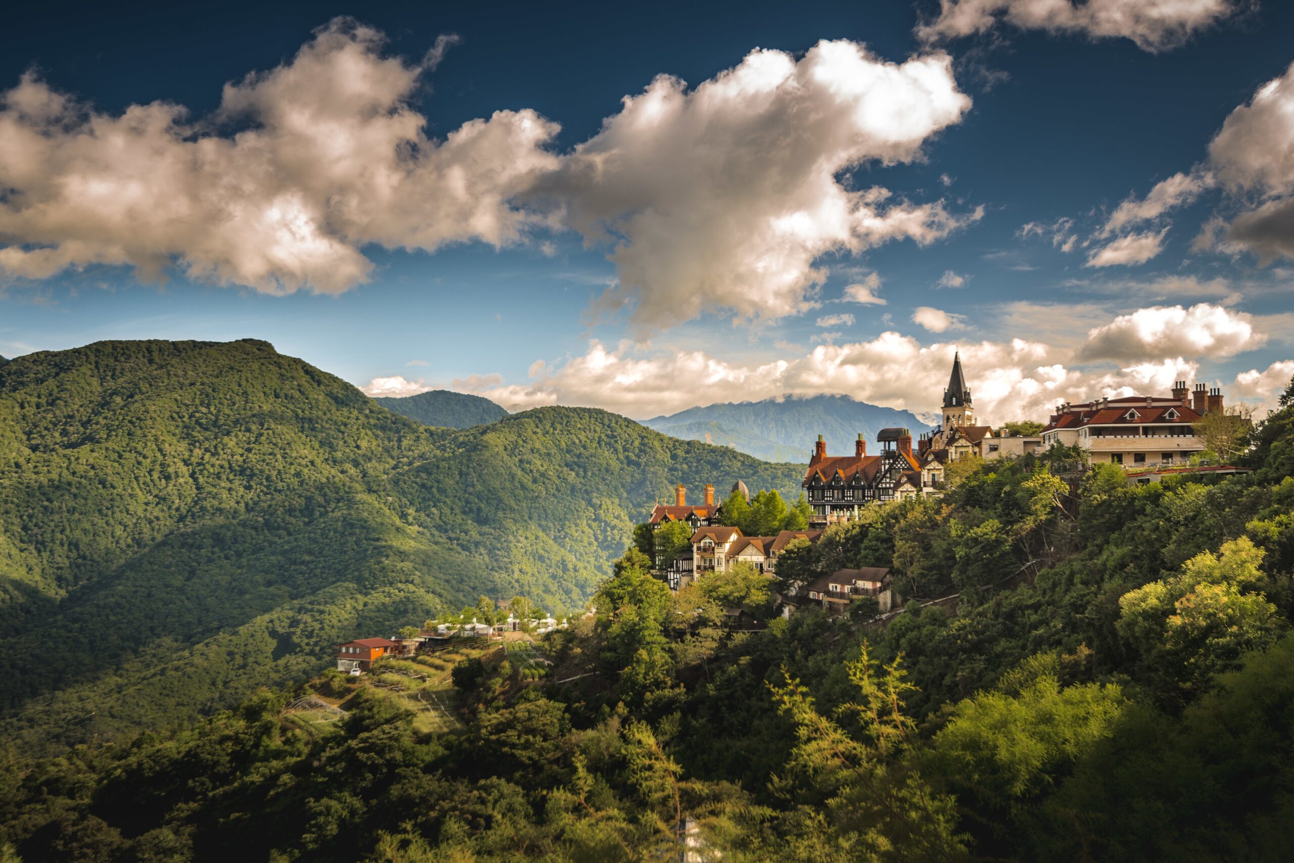 An aerial shot of a small village on the hill surrounded by forested mountains
